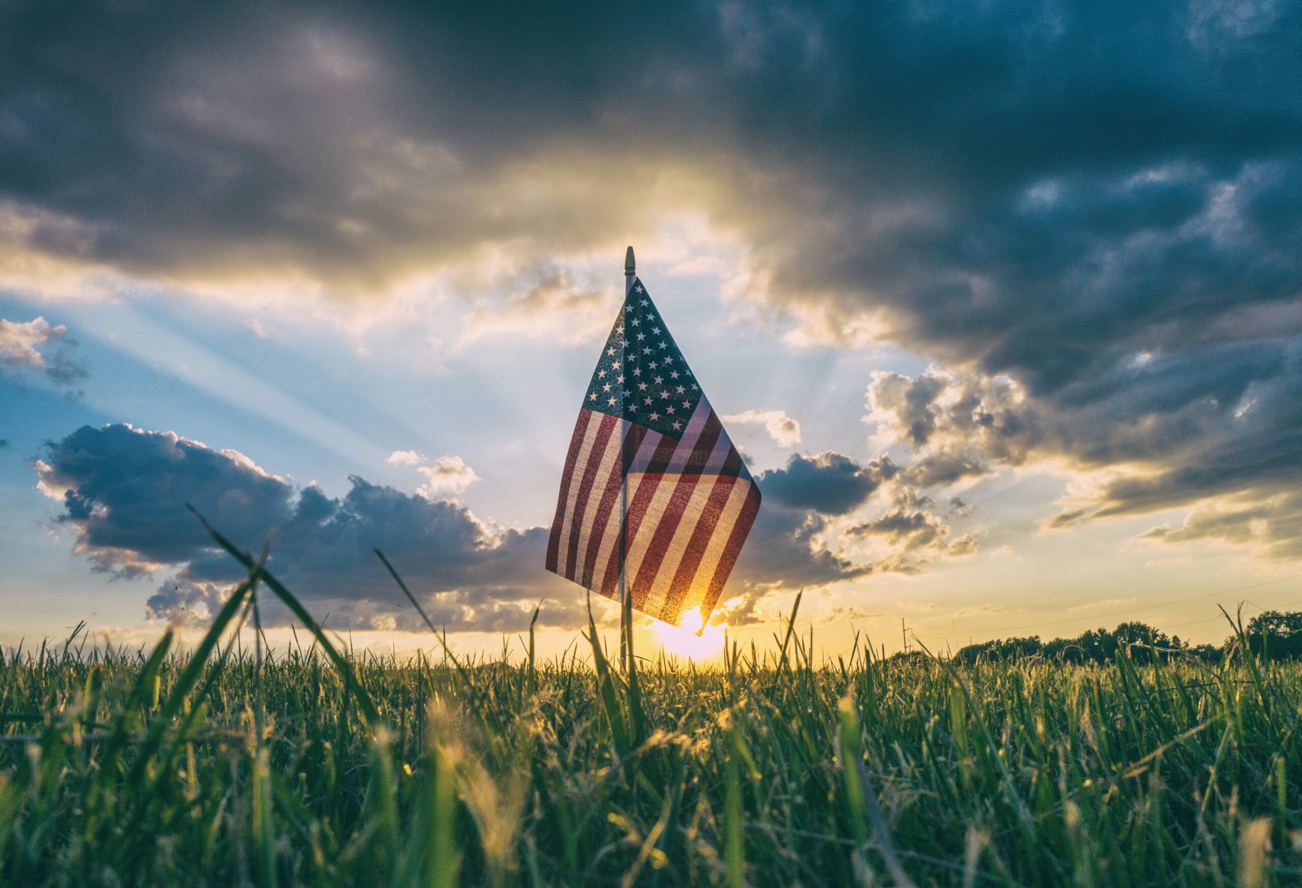 american flag in the middle of a field at sunset
